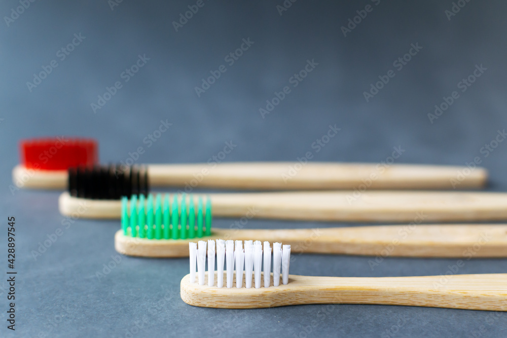 Four multi-colored bamboo toothbrushes lie on a gray background. Eco friendly stuff concept. Copy space. Horizontal orientation. Selective focus. Four multi-colored bamboo toothbrushes lie on a gray background. Eco friendly stuff concept. Copy space. Horizontal orientation. Selective focus.