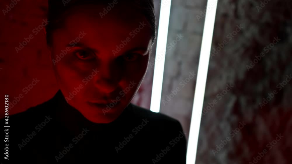 scary red light on face of adult woman in dark room, lady is looking at camera
