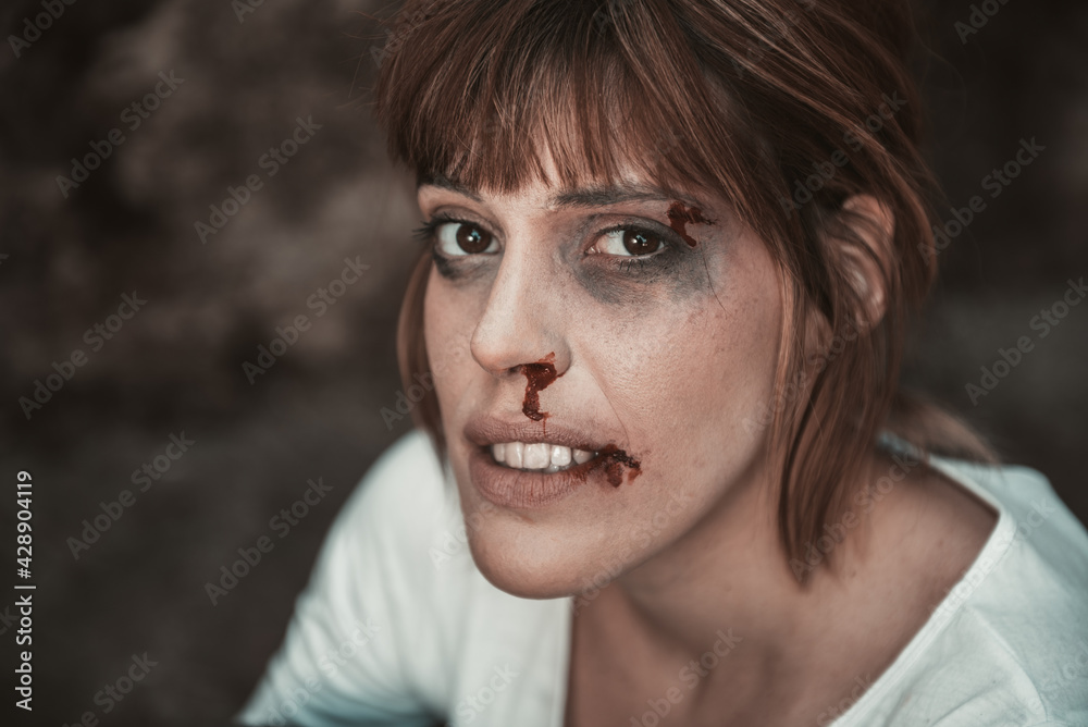 Close-up of a desperate woman in profile that she is suffering a violence, she have blood of the nose and the bruises under shattered eyes.