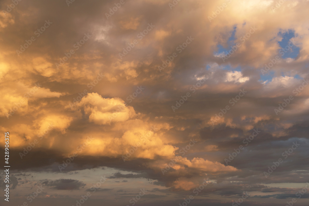 Epic sunset storm sky. Big white grey cumulus thunderstorm clouds in yellow orange sunlight on blue sky background texture