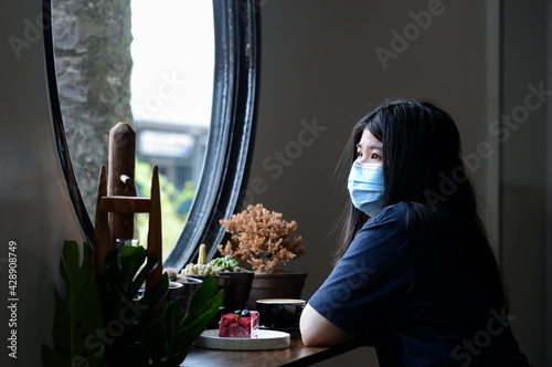 A woman wear sugical mask sits look out of the window. Lonely lady wear protective medical mask sits near the window at home for protection from covid-19. State Quarantine. health, safety and pandemic photo