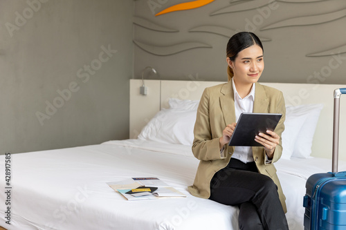Young attractive female traveler using tablet to get information for her direction or place for dining around. Smiling young visitor checking news or business messages online in a clean apartment room