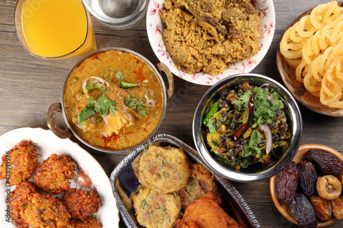 Bengali Iftar Ramadan breakfast spread ripe dates peep fried spicy piaju onion fitter eggplant tanpura potato chop haleem jilapi khichuri rice chana sola curry on rustic wooden table