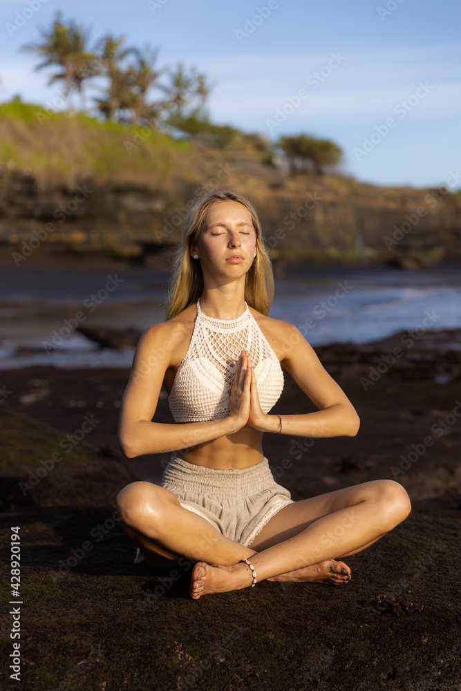Beautiful woman practicing yoga on the beach. Sitting in Padmasana, Lotus Pose. Hands in namaste mudra. Positive energy. Healthy life concept. Yoga retreat. Beach in Bali.