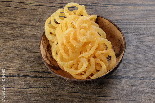 Jalebi Jilapi zulbia mushabak zalabia deep frying maida white flour batter pretzel circular shapes soaked in sugar syrup in coconut shell over rustic wood background photo