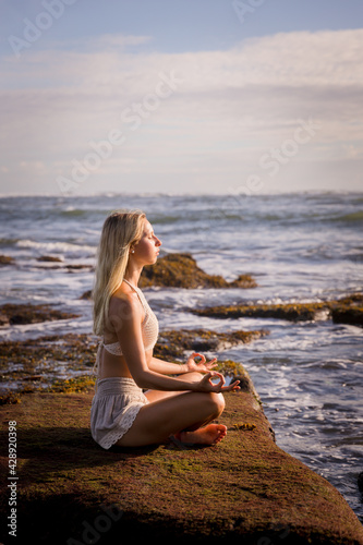 Woman practicing yoga on the beach. Sitting in Padmasana  Lotus Pose. Hands in gyan mudra. Positive energy. Healthy life concept. Yoga retreat. Copy space. Beach in Bali