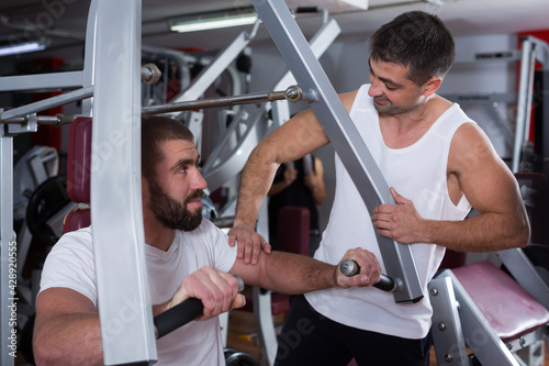 Portrait of sporty man during strength training with personal instructor in gym