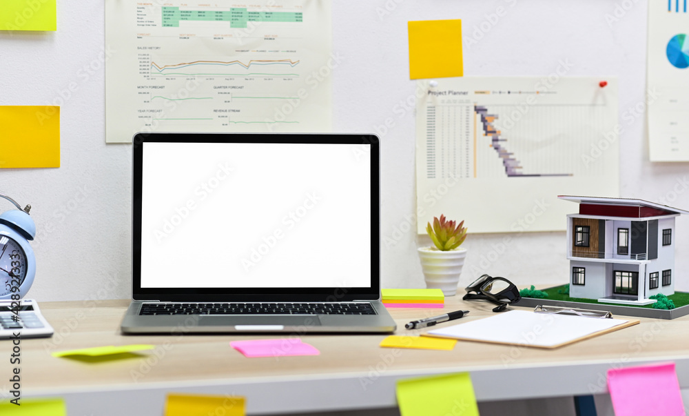 Blank screen laptop mockup with clipboard, model house with office supplies on the table and graph data on the wall. Blank screen laptop mockup with clipboard, model house with office supplies on the table and graph data on the wall.