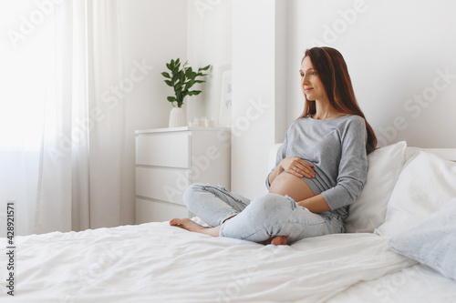 Young beautiful pregnant woman sitting on bed with white linen.
