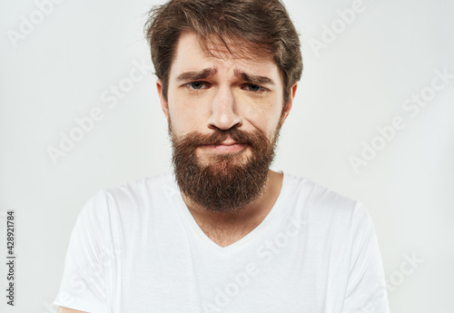 Bearded man in a white T-shirt on a light background sad face emotions beard