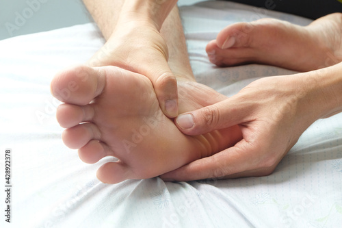Foot Pain ,young man sitting on the bed at home, he holding feet press massage . Concepts of pain and health therapy.