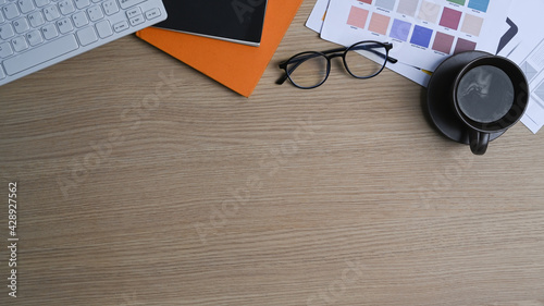 Top view of graphic designer work table with coffee cup  glasses  keyboard  notebook  color swatch and copy space.