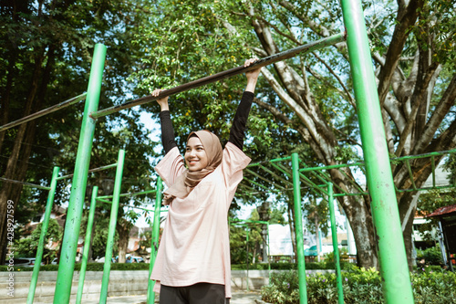 a girl in veil doing pull up to improve lung ability and lose weight by exercising outdoors in the park