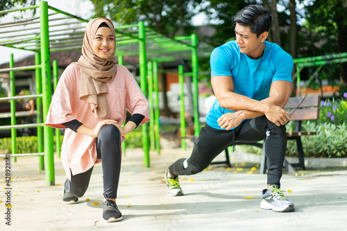 a man and a girl in a veil in gym clothes doing lunges movements while exercising outdoors together at park