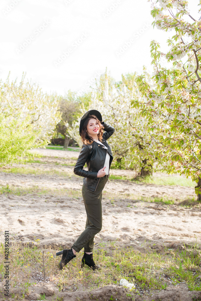 Lovely young girl in a black hat and a fashionable black leather jacket in spring in a blooming cherry garden in sunny weather with a blooming cherry branch in her hands. Spring and Fashion
Lovely young girl in a black hat and a fashionable black leather jacket in spring in a blooming cherry garden in sunny weather with a blooming cherry branch in her hands. Spring and Fashion