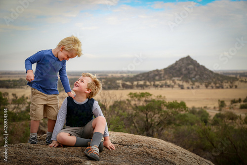 Little boys sitting on rock during bushwalk with view of Pyramid Hill, Victoria Australia in the background. Nature walk on a cloudy day.