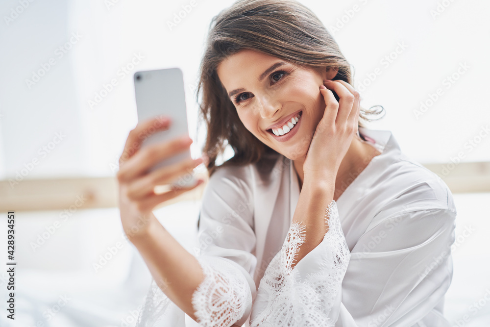 Happyadult woman using smartphone in bedroom in the morning Happyadult woman using smartphone in bedroom in the morning