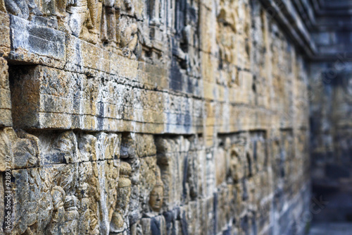 Interior of ancient Borobudur temple lower terraces. Close up of detail stone reliefs on the wall in corridor with bokeh background. No people. For wallpaper or background. Popular tourist destination