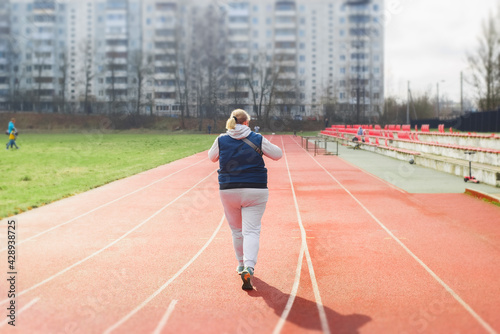 Plus size woman jogging in the stadium, outside. Active lifestyle, weight loss concept. Back view