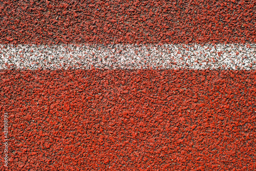 White line on the red running track at the stadium outside, close-up. Sports textured background top view. Finish, start concept