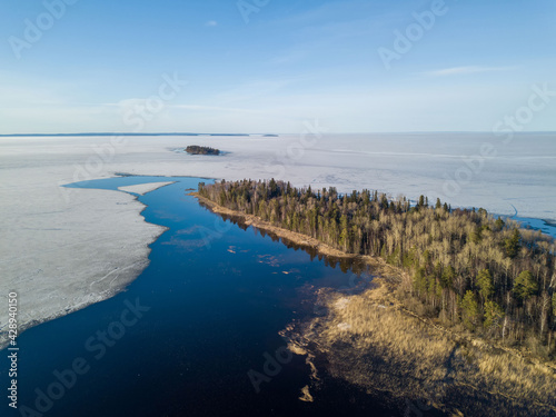 Aerial view of the large Onega Lake in Karelia (northwest Russia) with melting ice and big area of open water near the coast and the island. Forest by the lake. Sunny, spring day