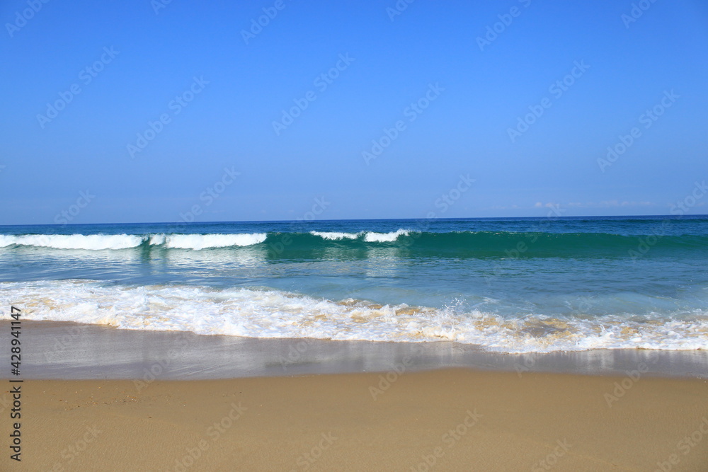 Une vague avec de l´écume blanche déferle vers la plage de sable , il fait beau, le ciel est bleu.