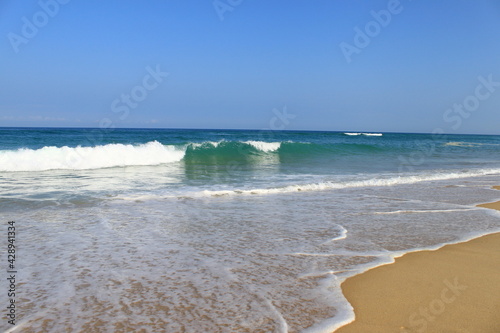 Une vague avec la mousse blanche avance vers la plage de sable jaune. L´océan est bleu vert et le ciel est bleu sans aucun nuage.
