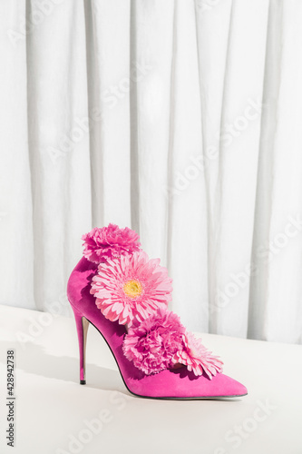 Minimal sustainable fashion concept with pink high heel and pink daisy and carnation flower on beige background. Cream aesthetic summer creative idea. Environmental protection.