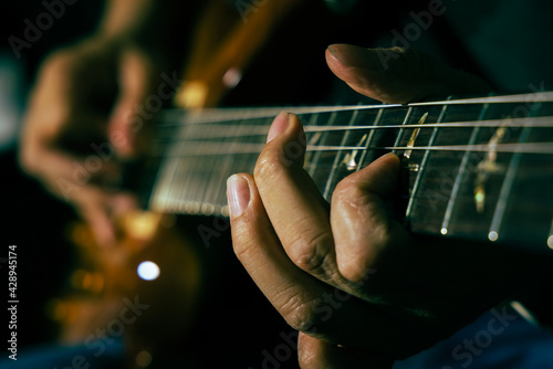 Closeup of man guitarist's hand and finger during pushing the string on the guitar neck for chord while playing electric guitar solo. Song practice.