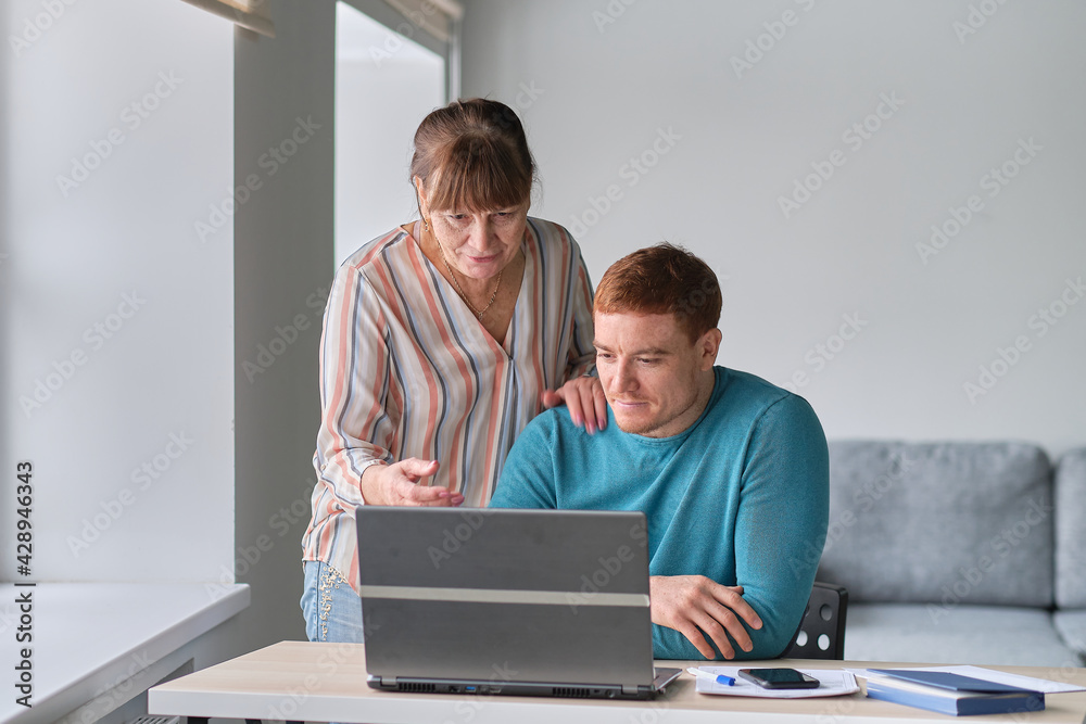 Young Man showing how to use computer to an old woman. elders technology concept. Middle aged man helping his mother use a laptop computer at home, close up Young Man showing how to use computer to an old woman. elders technology concept. Middle aged man helping his mother use a laptop computer at home, close up