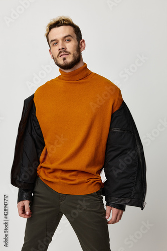 sexy man in sweater and leather jacket posing on light background cropped view