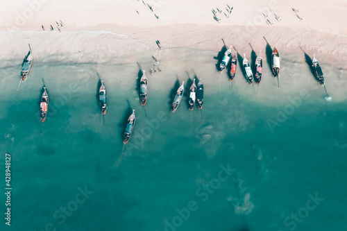 Aerial view of traditional longtail boats floating on a turquoise and clear ocean in Thailand.