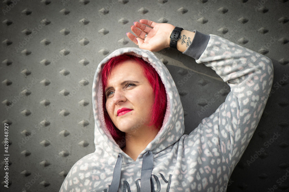 Naklejka premium Frau mit rotem Haar und Kapuzenpullover vor grauer Strukturwand