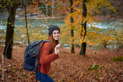 woman in a sweater with a backpack on her back near the river in the mountains and park trees autumn landscape © SHOTPRIME STUDIO
