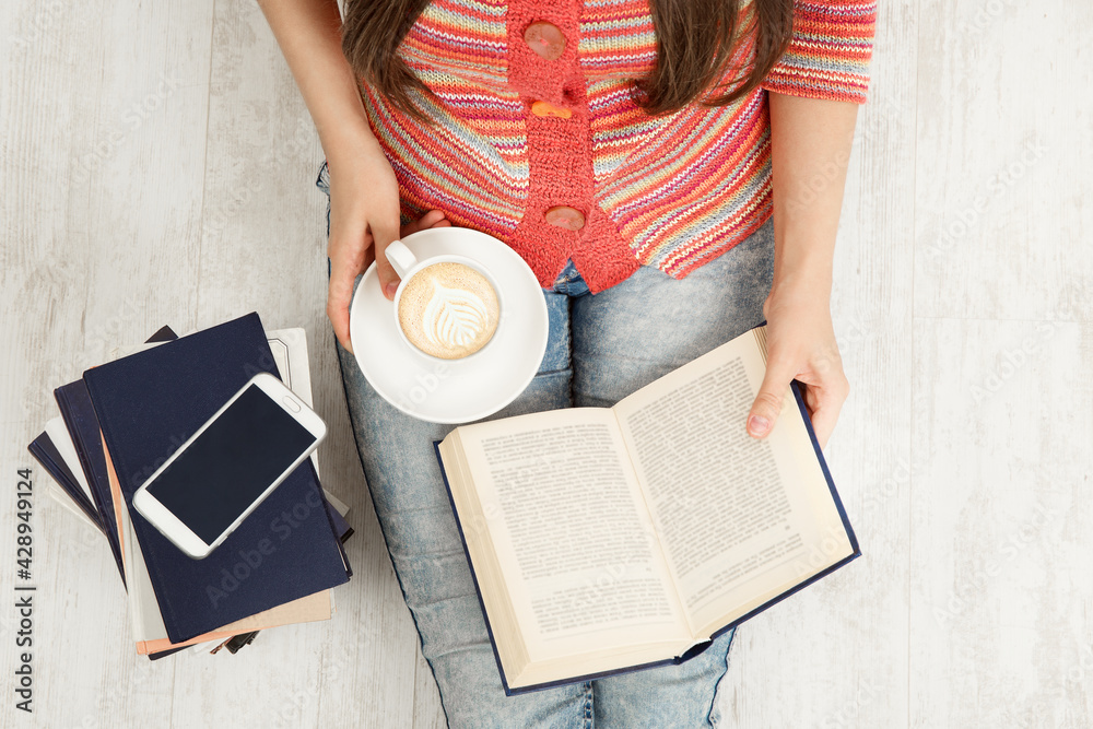 Obraz premium Close up Women Hands Holding Coffee Cup and Reading opened Book. Top view of Woman with Teacup having Break. Sitting Young Girl Study Books