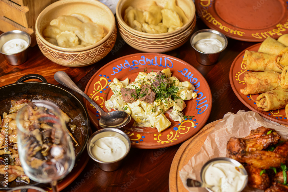 Potato salad with meat and mayonnaise sauce served on a ceramic plate on the table covered with other dishes.