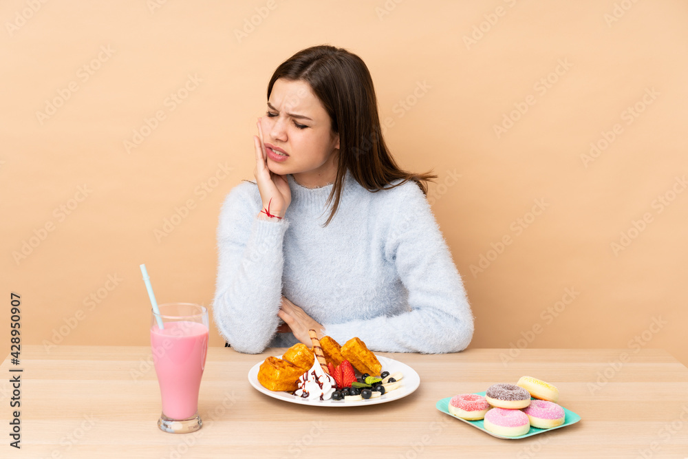 Teenager girl eating waffles isolated on beige background with toothache Teenager girl eating waffles isolated on beige background with toothache