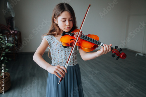 Little brunette girl in a beautiful dress playing violin indoors. Music instruments concept.