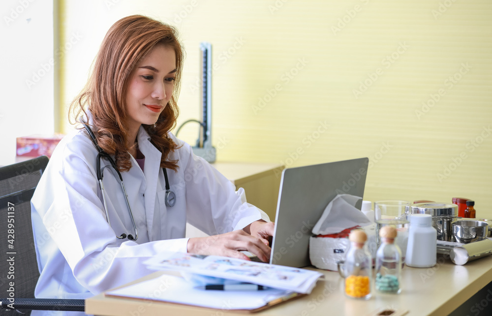 Close up of asian female doctor wearing white medical gown with stethoscope sitting at desk in hospital and concentrating on typing a prescription for patients. Healthcare, medicine concept. Close up of asian female doctor wearing white medical gown with stethoscope sitting at desk in hospital and concentrating on typing a prescription for patients. Healthcare, medicine concept.