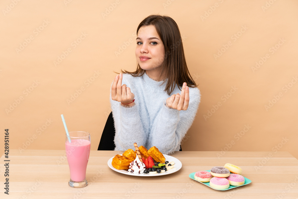 Teenager girl eating waffles isolated on beige background making money gesture Teenager girl eating waffles isolated on beige background making money gesture