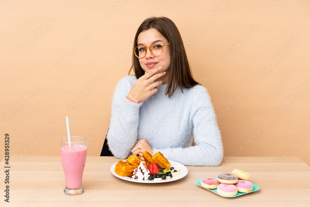 Teenager girl eating waffles isolated on beige background with glasses and smiling Teenager girl eating waffles isolated on beige background with glasses and smiling