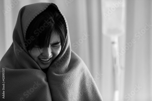 Fototapet Close-up of a severe sick young woman sitting on bed in the hospital, got a flu or cold and covered her body in green blanket to relieve from a frozen fever
