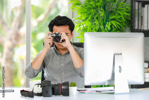 Close-up of a young professional photographer sitting in the office, hand holding a retro camera, taking pictures to test the focusing systems and new features.