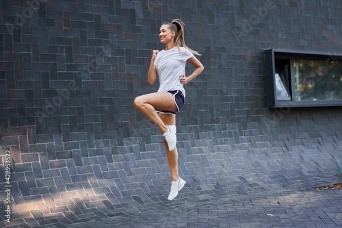Woman with fit body jumping and running against black wall background