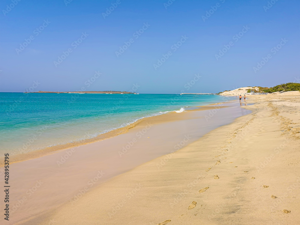 Summer mood on the beach in Cape Verde. Turquoise color of Atlantic Ocean, tourists in the distance and perfect tropical climate. Selective focus on the water, blurred background.