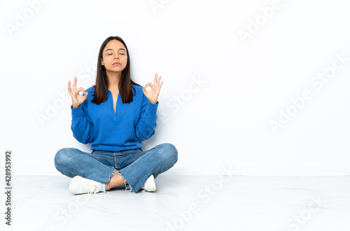 Young mixed race woman sitting on the floor isolated on white background in zen pose