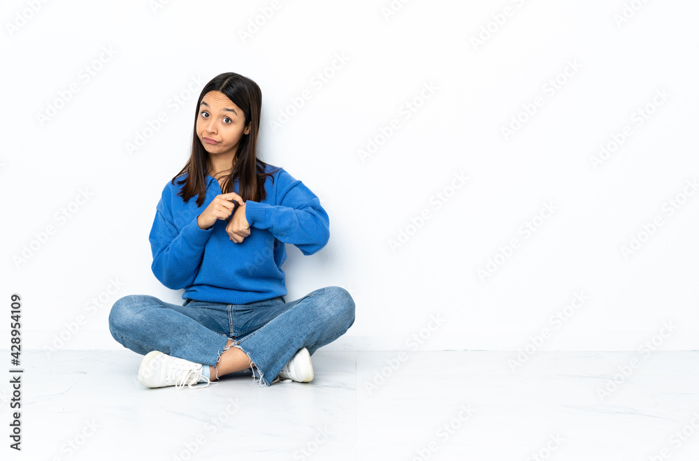Young mixed race woman sitting on the floor isolated on white background making the gesture of being late