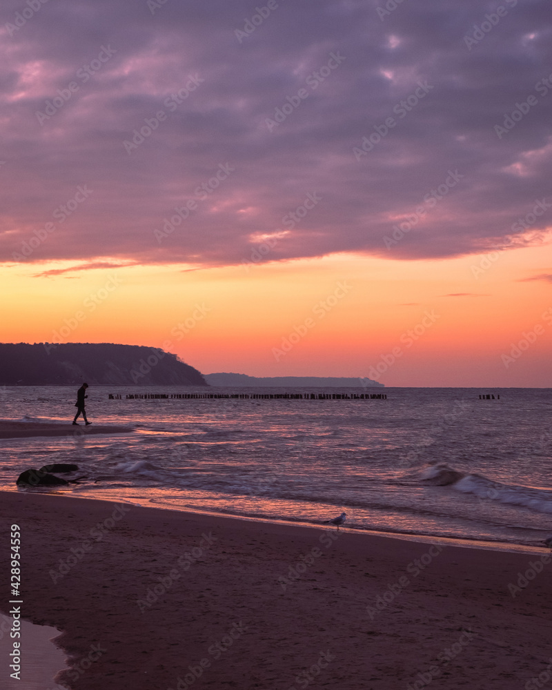 Sunset at the sea. Beautiful view on the beach and water, purple sky with clouds, vacation at Baltic sea. Sihouette of one person in the background. Ocean in the dusk. Breathtaking seascape.