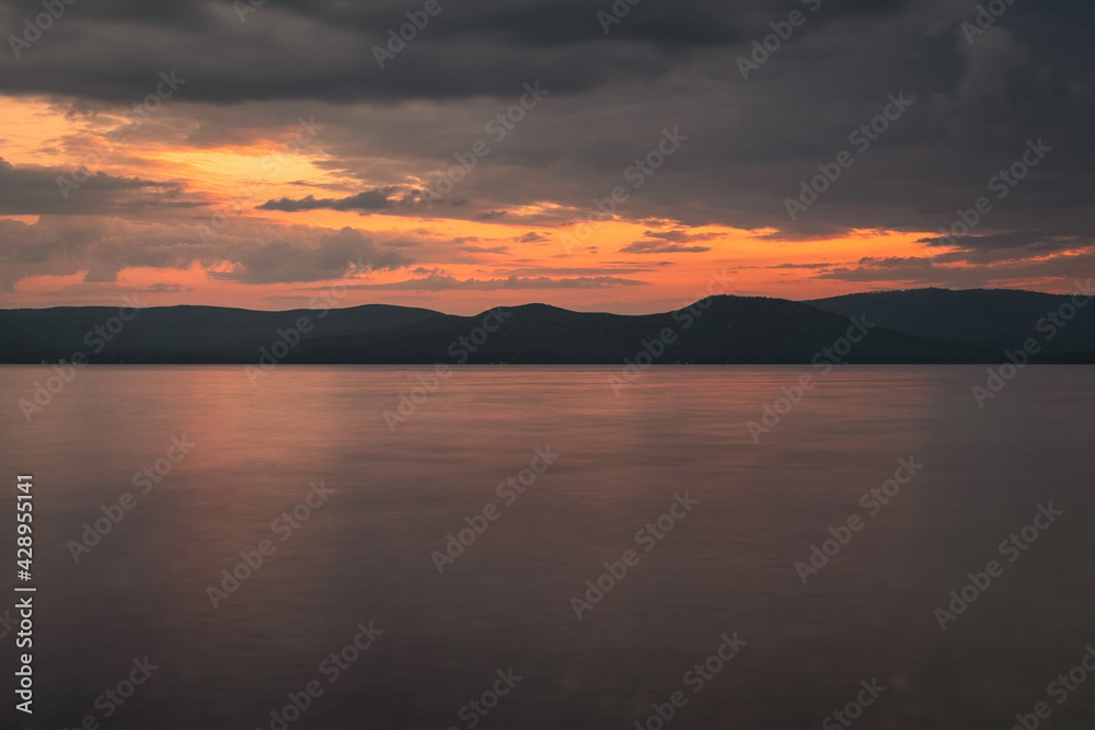 Photography of the sunset on the sea. Orange reflection on the water, mountains in the background. Dramatic view, breathtaking seascape. Golden sun rays.