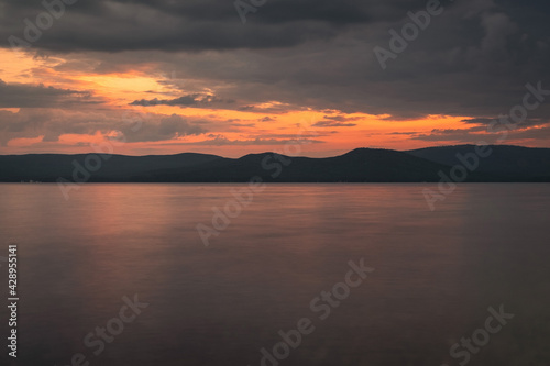 Photography of the sunset on the sea. Orange reflection on the water, mountains in the background. Dramatic view, breathtaking seascape. Golden sun rays. © Derariad
